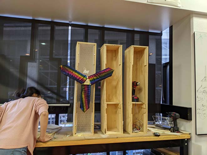 Plywood boxes lined up with a windmill blade attachment covered in metallic rainbow fabric.