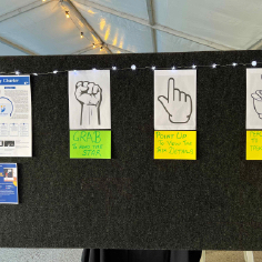 Galaxy Charter A3 poster and flyer, and grab, point and peace sign gesture images and its instruction prompts attached onto a divider wall at the exhibit